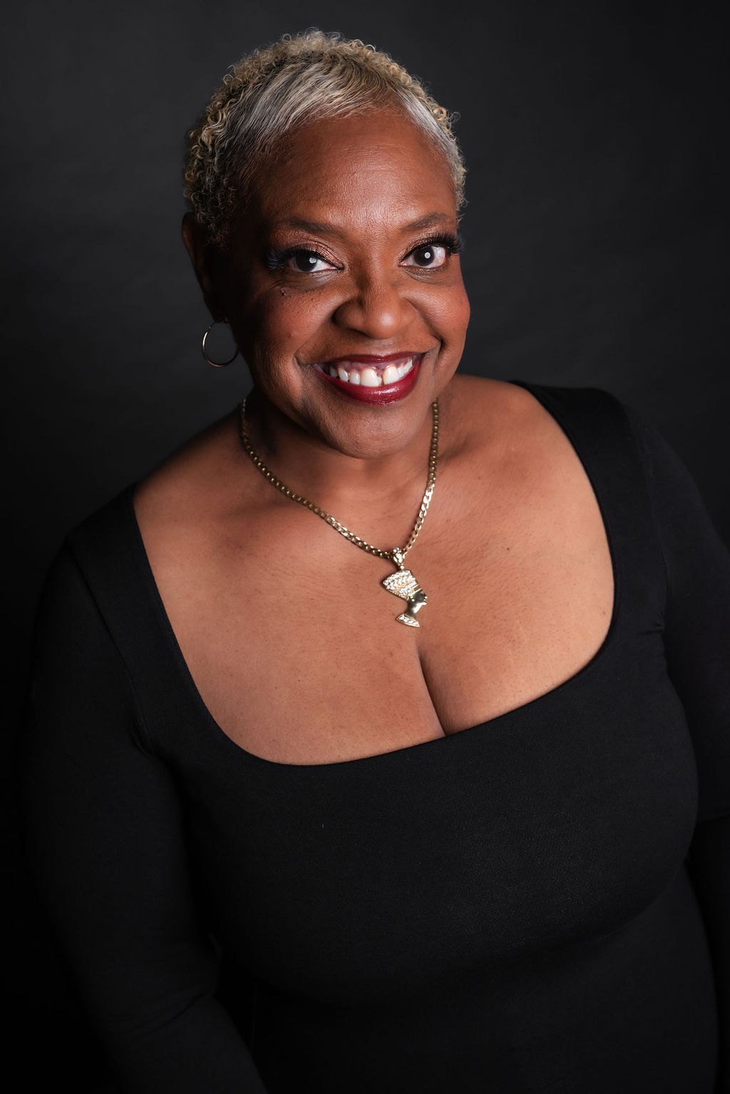 Ann James, founder of New Day Theatricals, smiling in a black dress against a dark backdrop